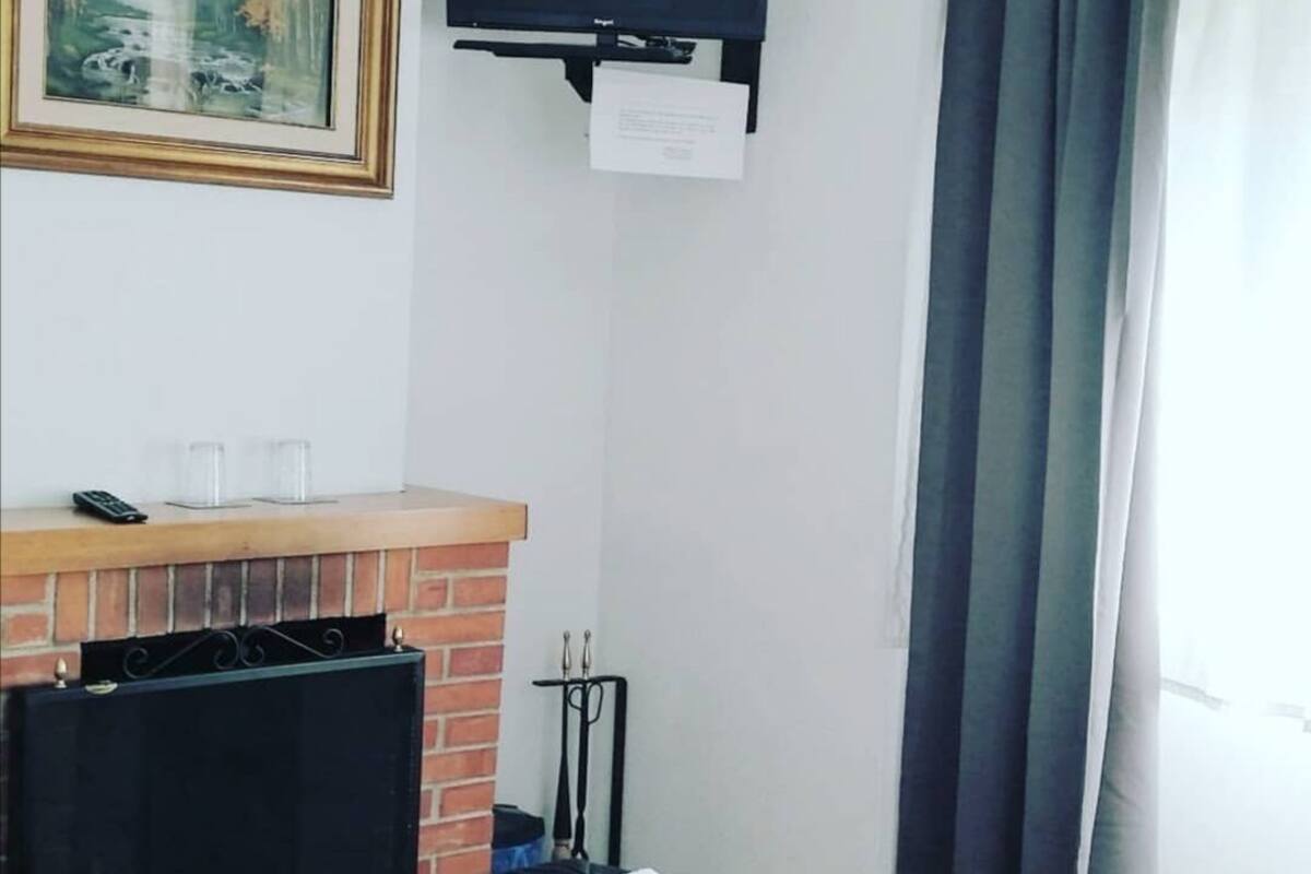 A hotel room with a fireplace, a bed, a TV mounted on the wall, and a painting on the wall.