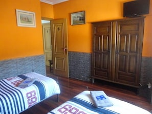 A hotel room with two beds, a wardrobe, and a television on the wall. - Pensión Txoko-Maitea (Urnieta)