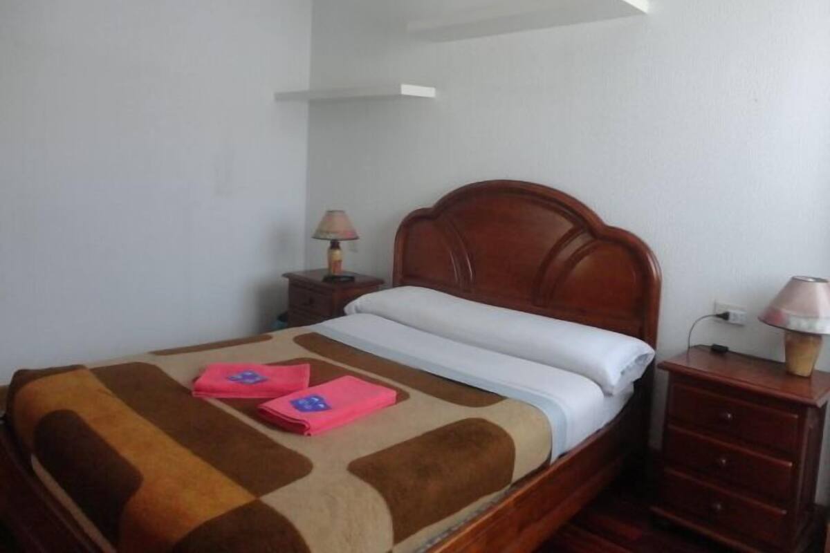 A neatly made bed with a brown headboard, a bedside table with a lamp, and a small drawer.