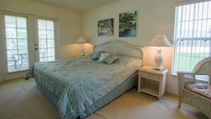 Un dormitorio con una cama, dos mesitas de noche, una silla y una puerta con ventanas.