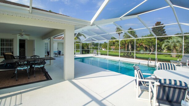 Zona de piscina exterior techada con patio, sillas y vistas del paisaje circundante.