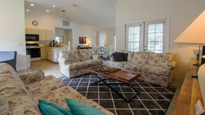 Amplia sala de estar con dos sofás de estampado floral, una mesa de centro y una cocina al fondo.