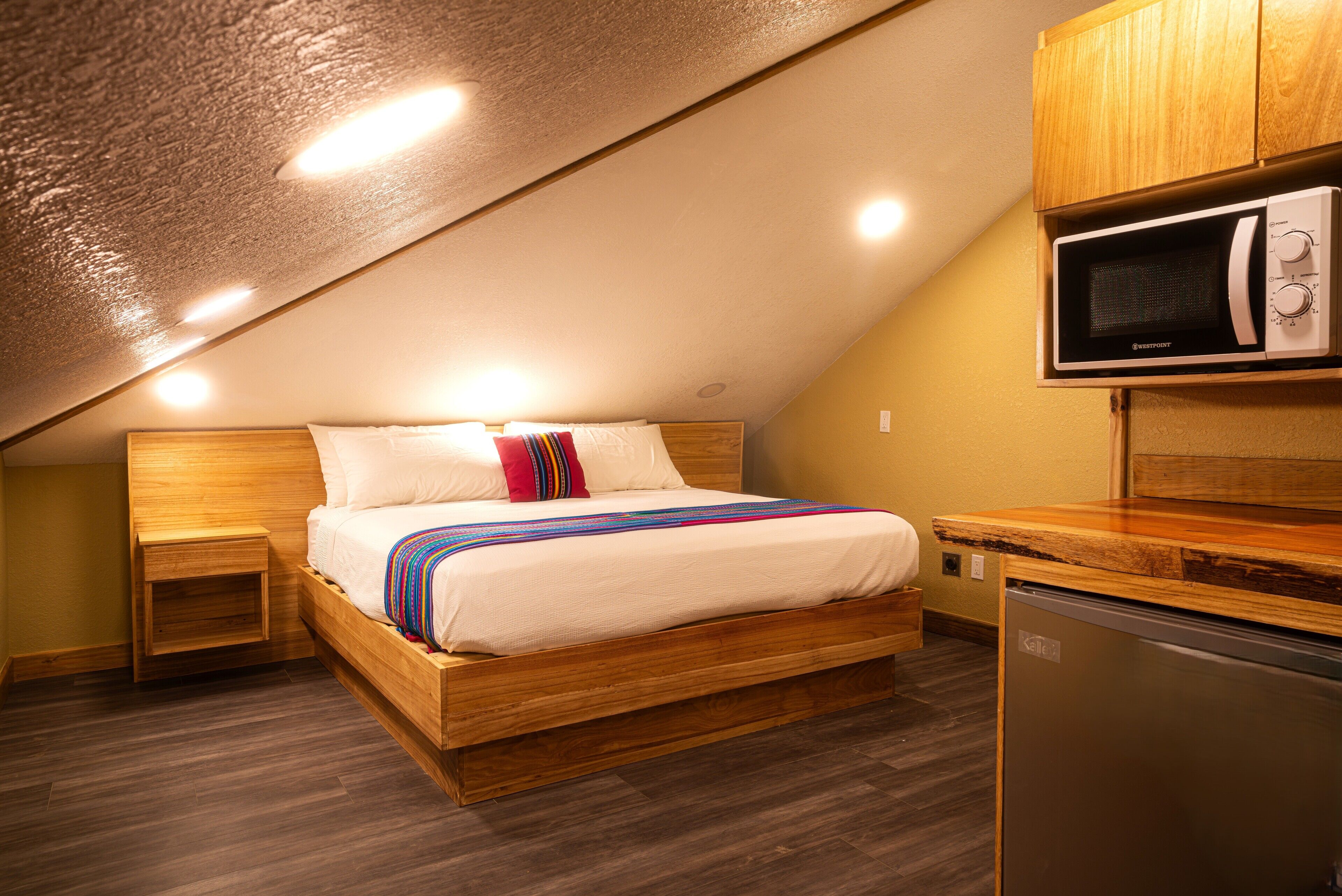 Un dormitorio con una cama de madera, un microondas empotrado y un refrigerador.