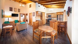 A spacious living area with a wooden ceiling, a dining table with chairs, a sofa, and a television.