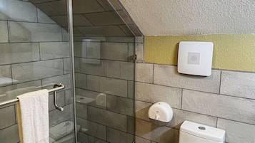 A modern bathroom with a glass-enclosed shower, a toilet, and a hand dryer.