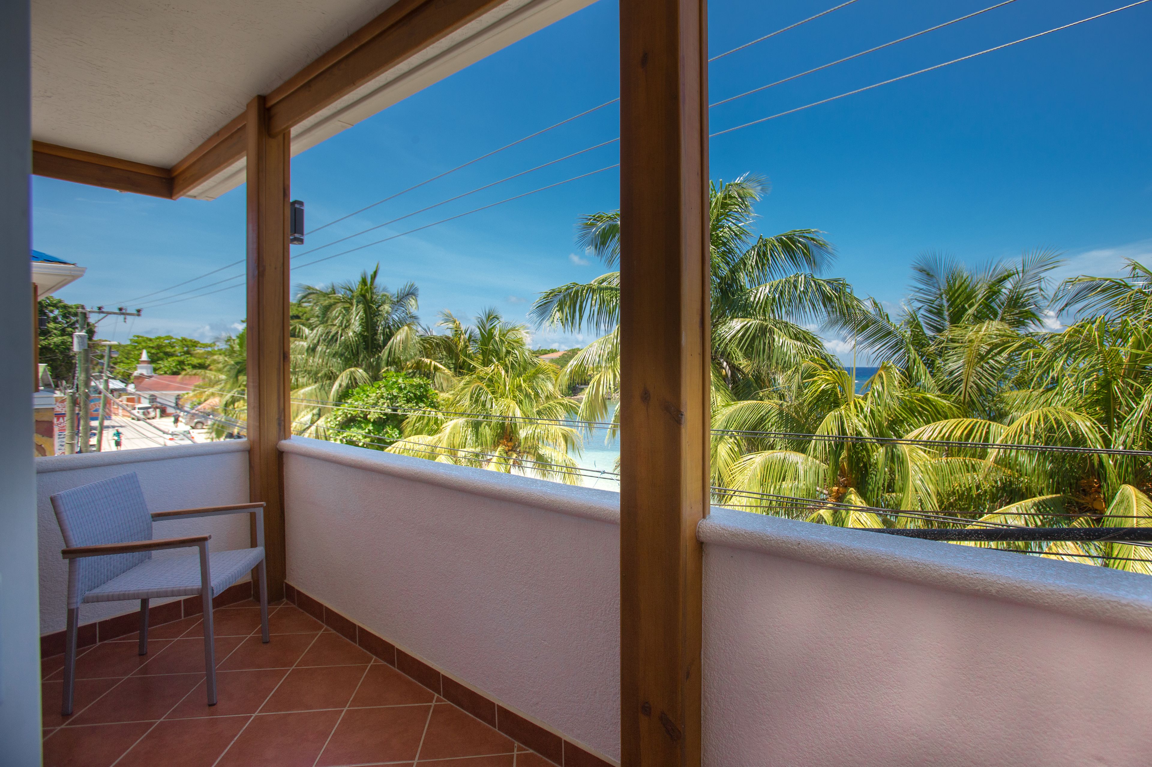 Un balcon avec une chaise, une vue sur des palmiers et un ciel dégagé.