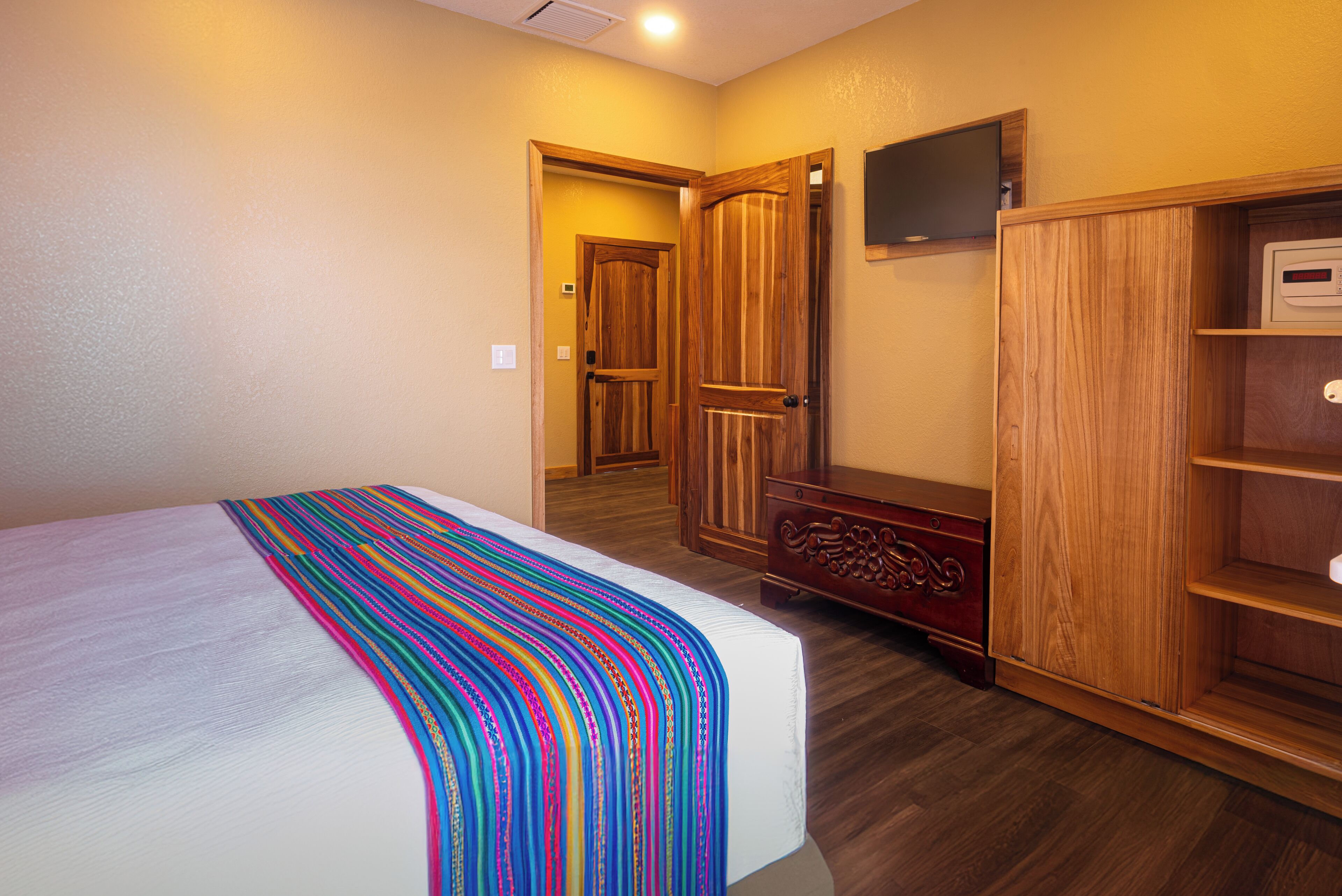 A bedroom with a bed, wooden wardrobe, and a television on the wall.