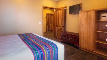 A bedroom with a bed, wooden wardrobe, and a television on the wall.