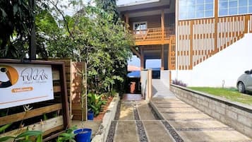 A hotel entrance with a signboard, a paved pathway, and a wooden building with a balcony.
