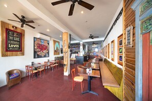 A restaurant with wooden tables and chairs, ceiling fans, and a bar area. - Mr. Tucan Hotel (Roatan)