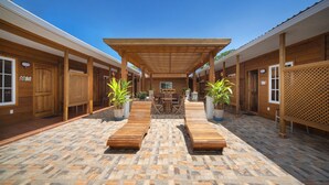 A covered outdoor area with wooden benches, potted plants, and a central table with chairs.