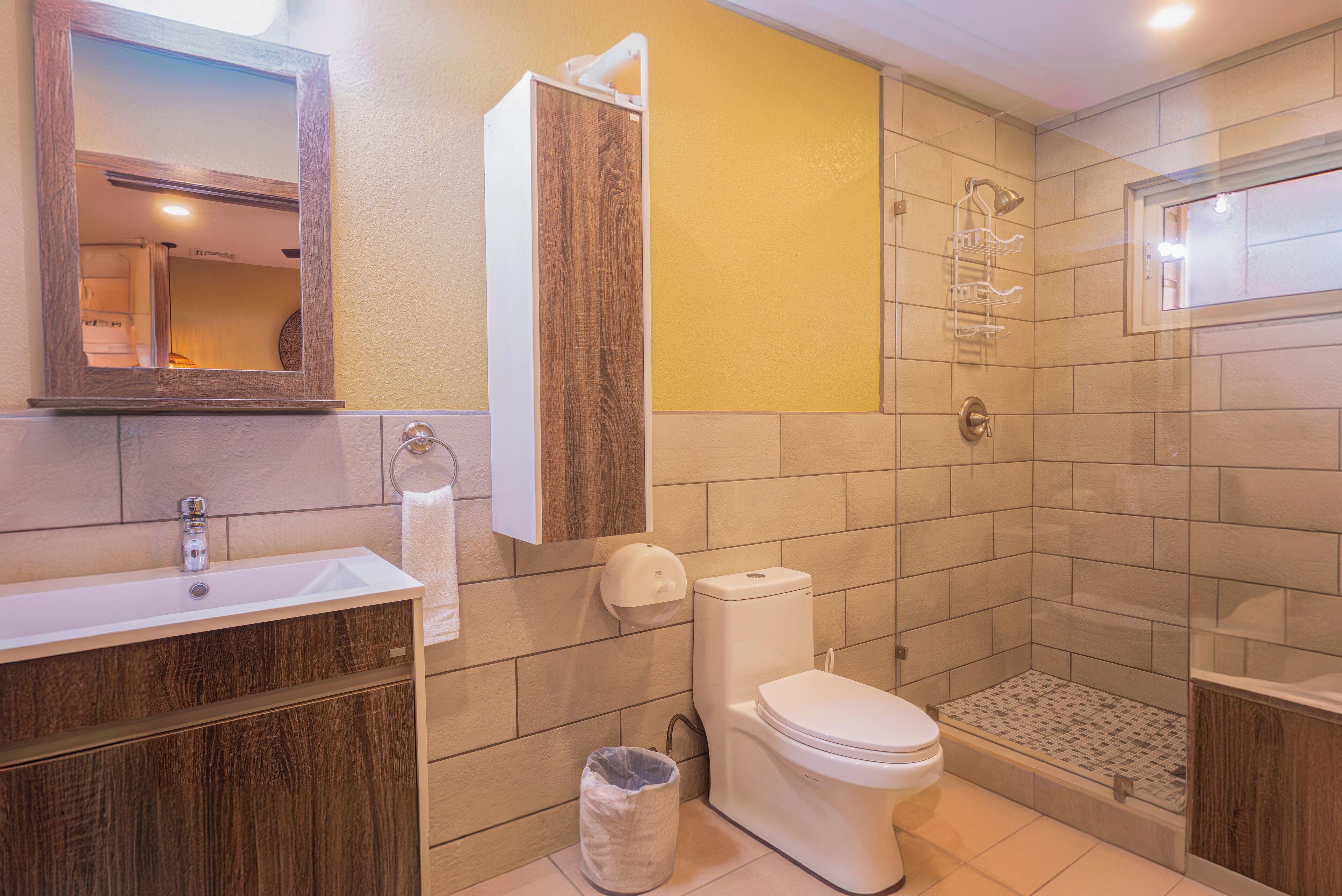 A bathroom with a wooden vanity, a toilet, a shower area, and a mirror.