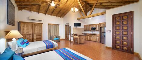 A room with two beds, a kitchenette, and a wooden ceiling.