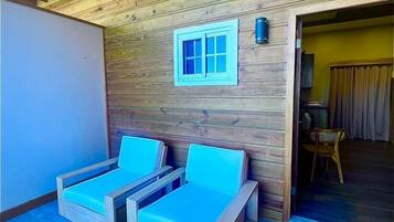 A room with two wooden-framed beds with blue cushions, a wooden ceiling, and a small window.