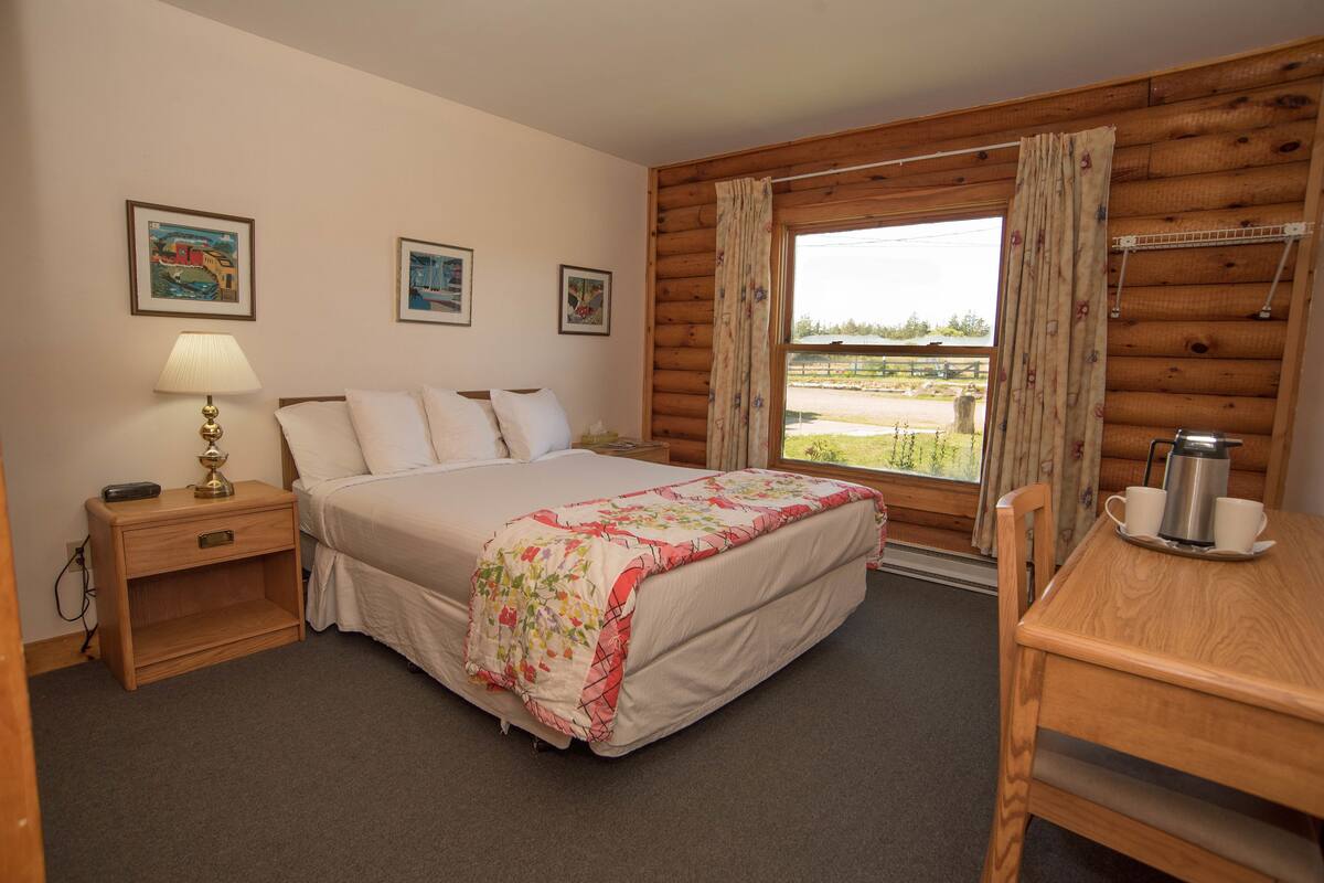 Quarto com cama, mesa de cabeceira, abajur e vista para o exterior.