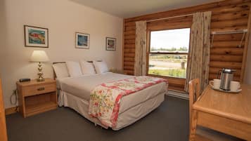 Un dormitorio con cama, mesita de noche, lámpara y vistas al exterior.