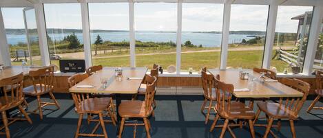 Un restaurant doté de grandes fenêtres offrant une vue panoramique sur un lac et des espaces verdoyants.