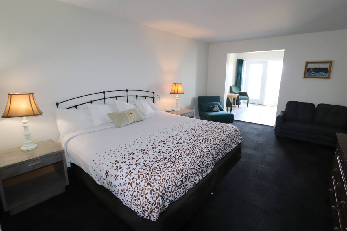 Quarto de hotel com cama, duas luminárias de cabeceira, uma poltrona, um sofá e vista para o exterior.