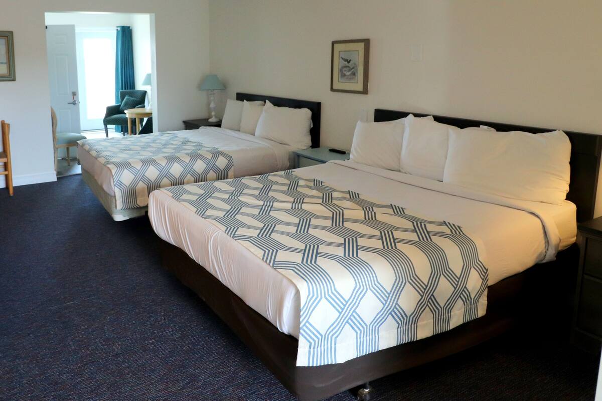 Quarto de hotel com duas camas, uma cadeira, uma escrivaninha e um abajur.