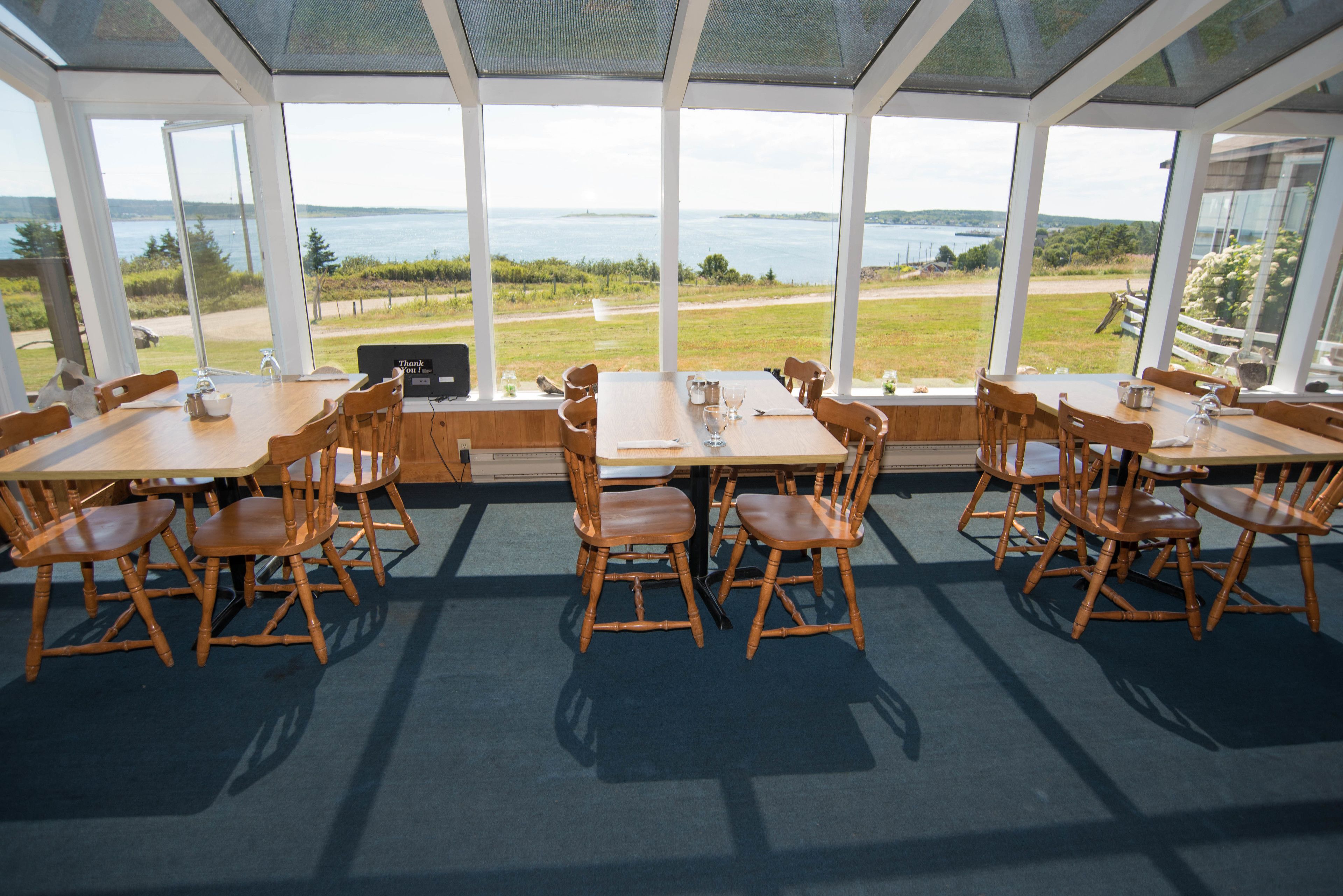 Un comedor con mesas y sillas, amplias ventanas que ofrecen vistas al mar y al paisaje.