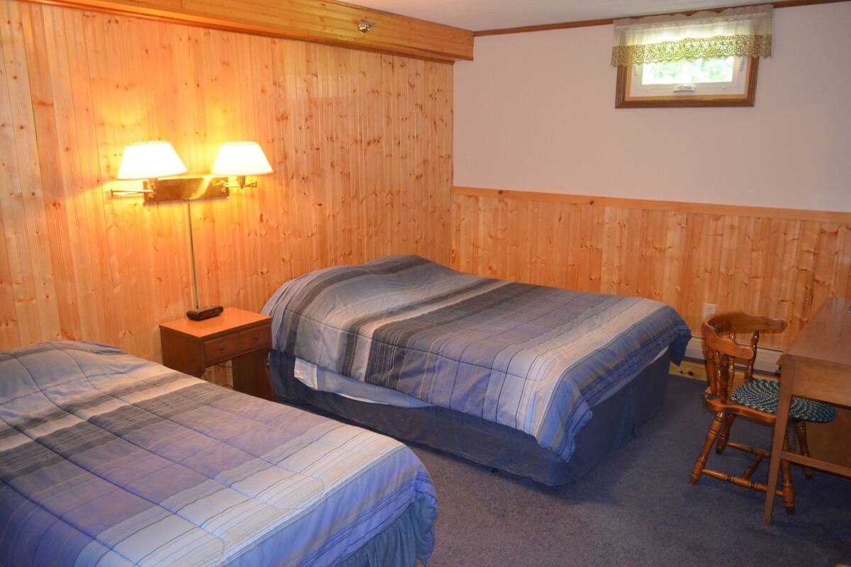 A room with two beds, a wooden wall, a small table, and a chair.