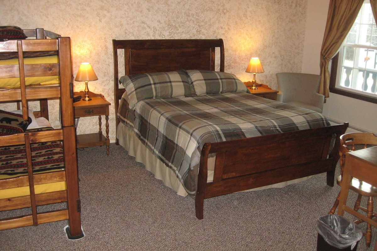 A bedroom with a wooden bed, two bedside lamps, a chair, and a window with curtains.