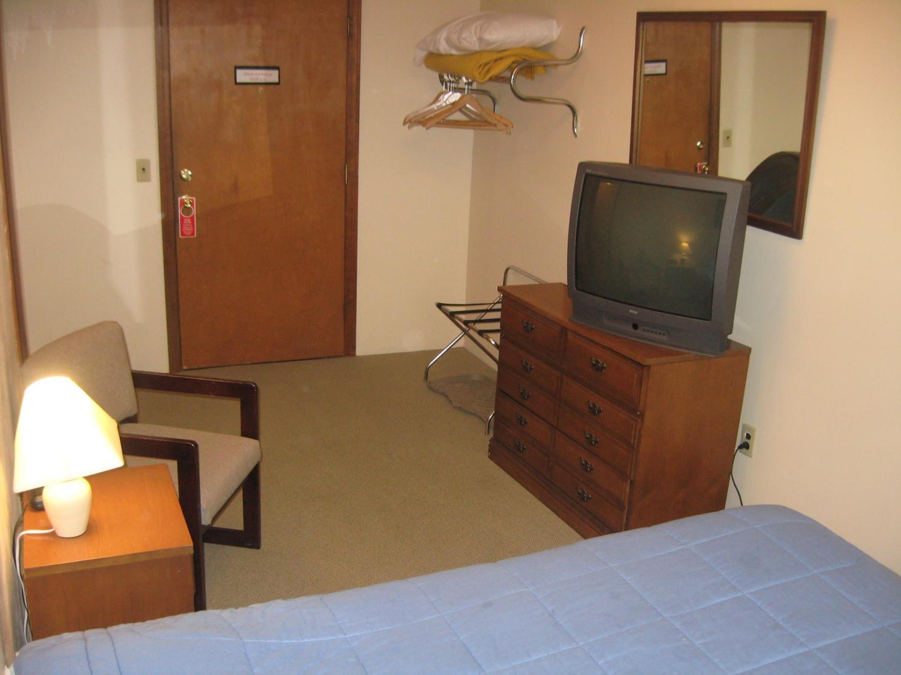 A hotel room with a bed, a wooden dresser with a television, a chair, a lamp, and a mirror on the wall.