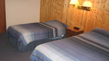 A hotel room with two beds, wooden panel walls, and two wall-mounted lamps.