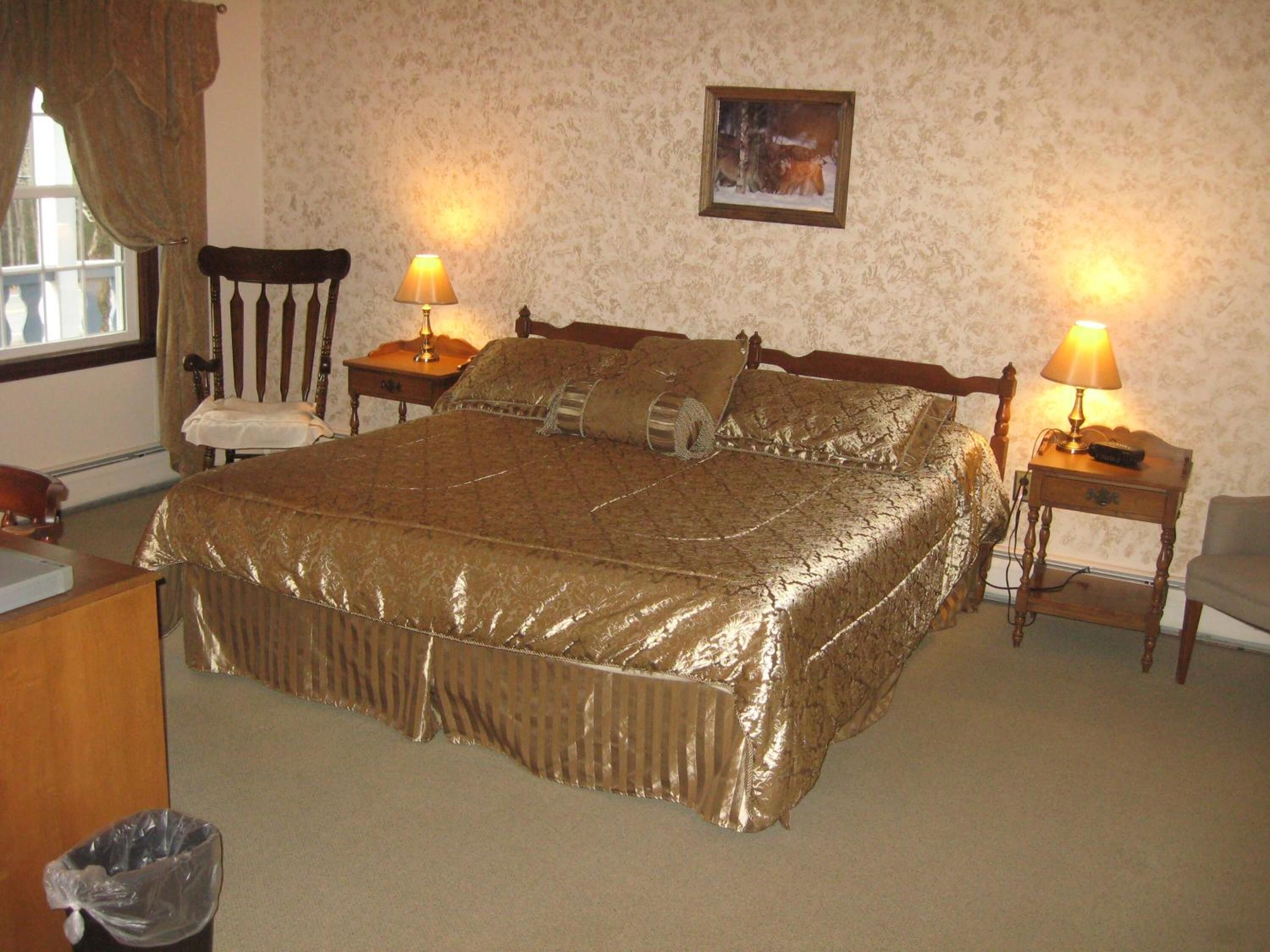 A neatly arranged bedroom with a large bed, two bedside tables with lamps, a chair, and a picture on the wall.