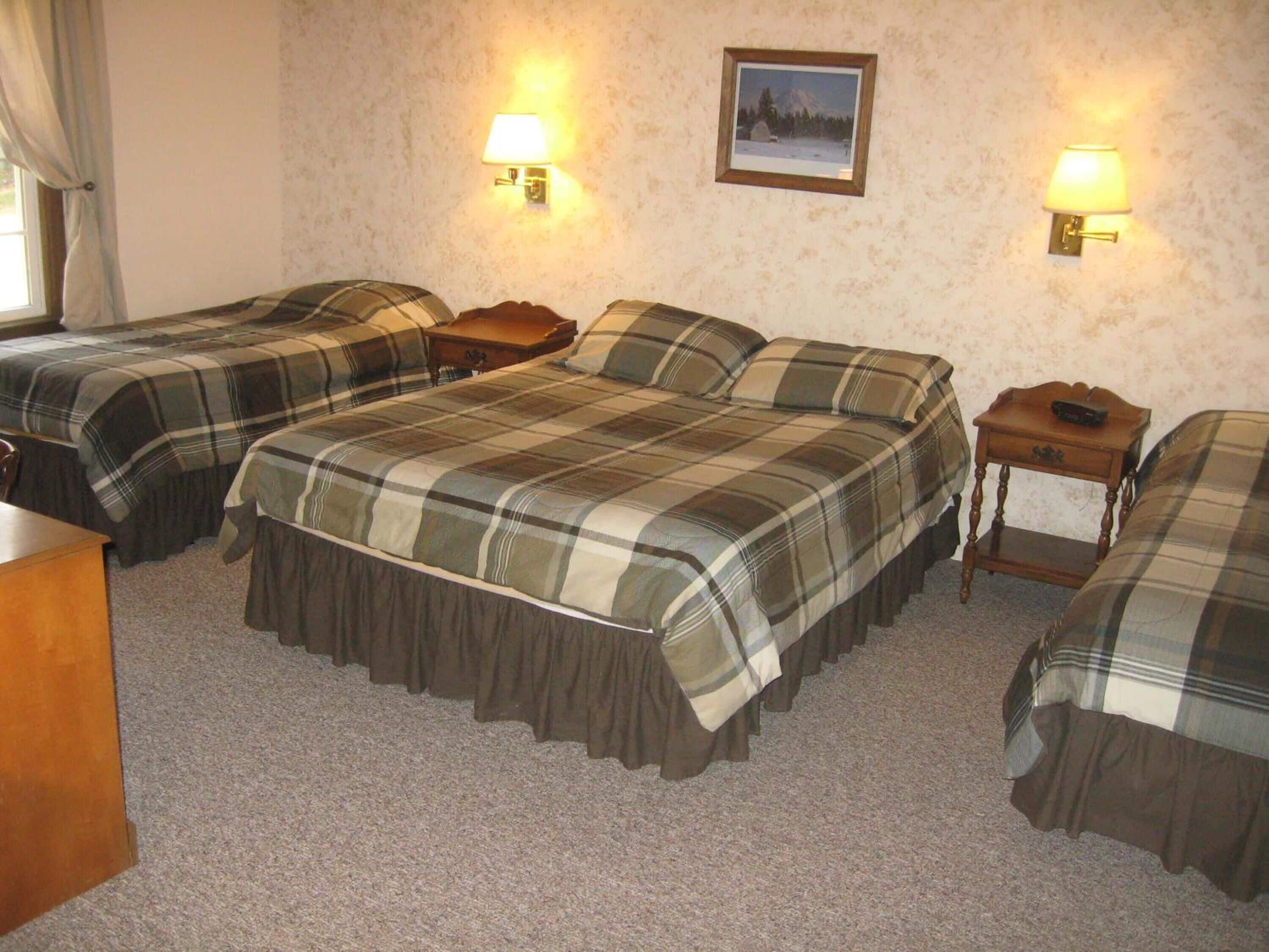 A hotel room with two beds, each with a plaid bedspread, two bedside lamps, and a framed picture on the wall.