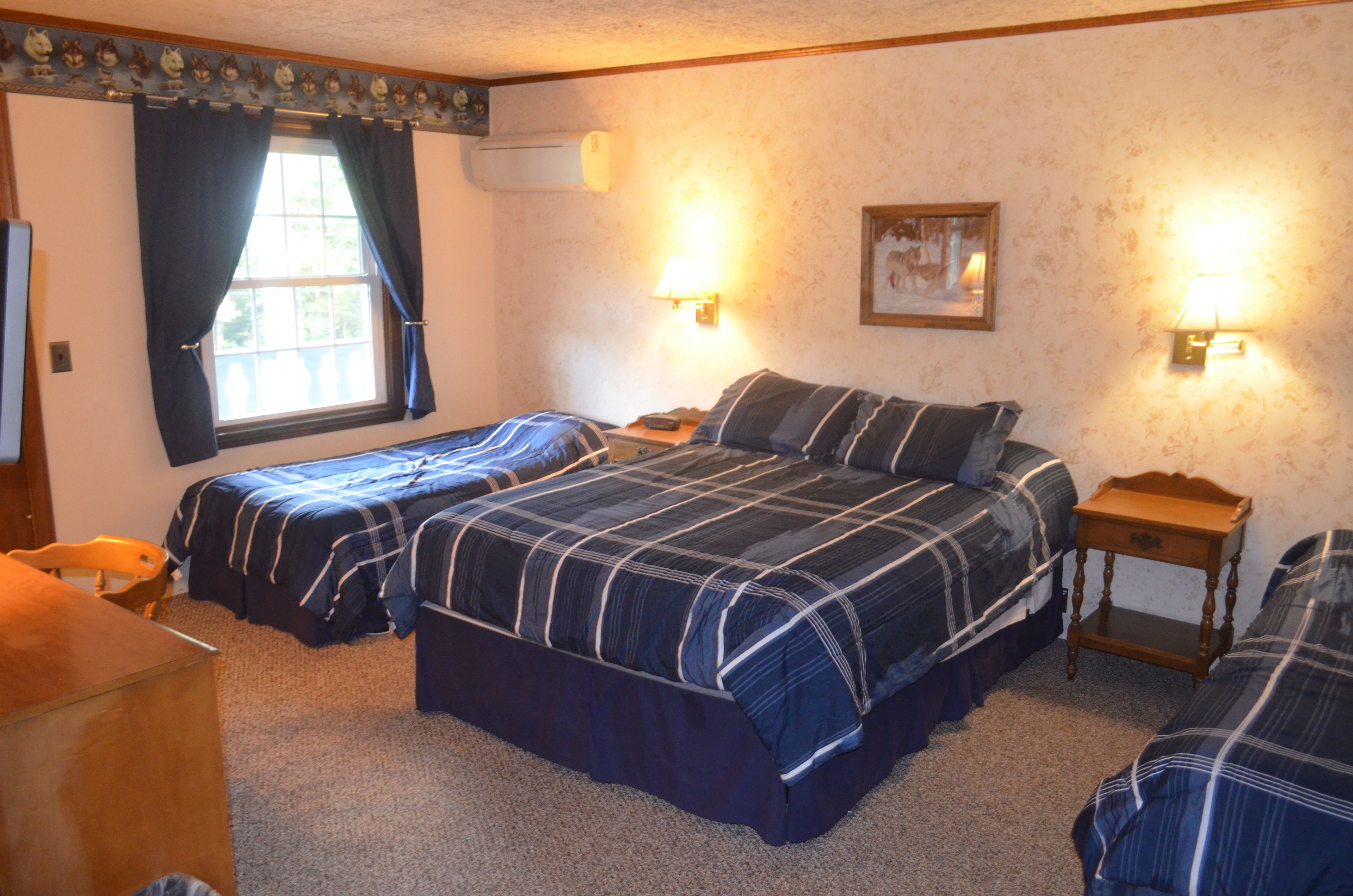 A room with two beds, a wooden desk, a chair, and a window with curtains.