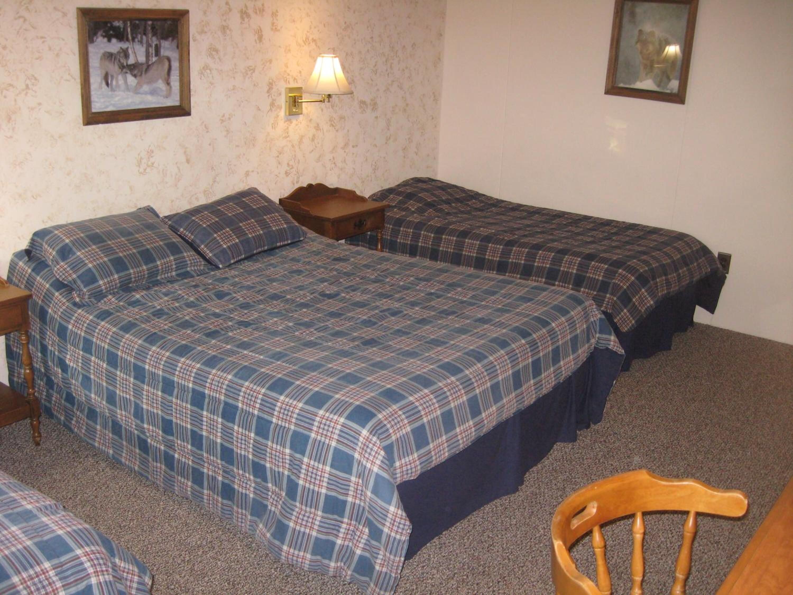 A room with two beds, a nightstand, a lamp, and a chair.