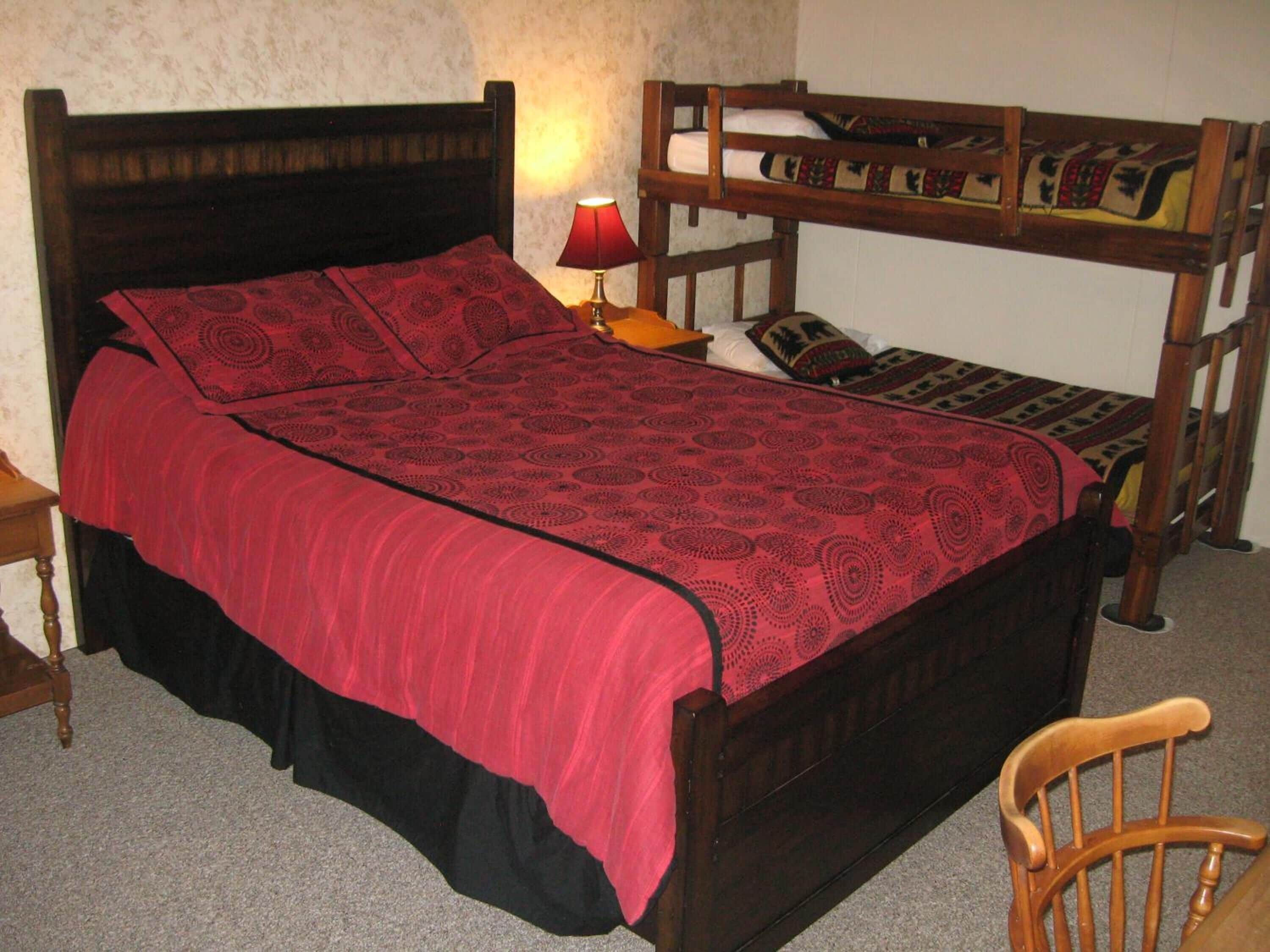 Una cama con una colcha roja estampada, un cabecero de madera y una mesita de noche con una lámpara.