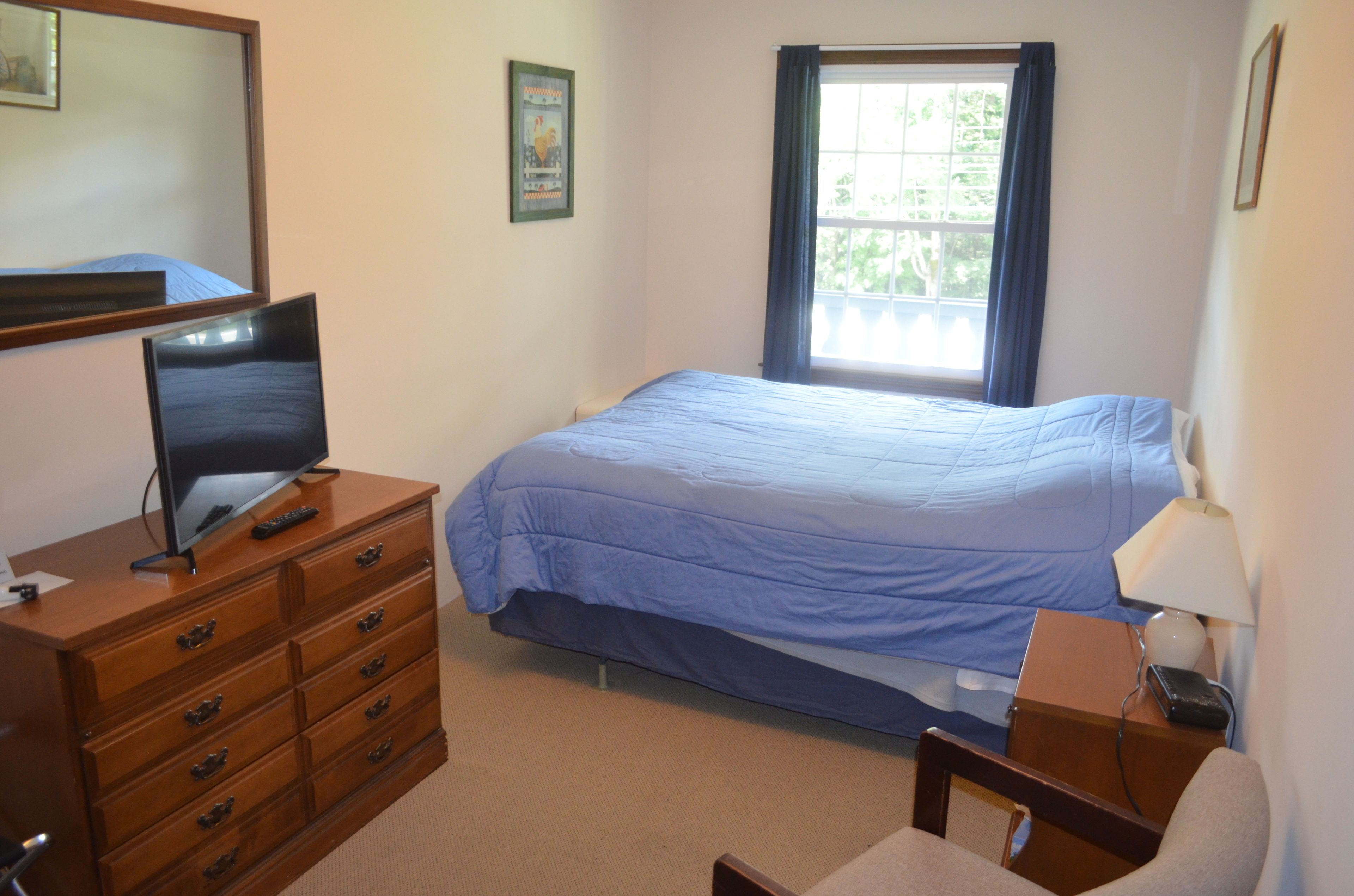 A bedroom with a bed, a dresser, a desk, a lamp, and a window.