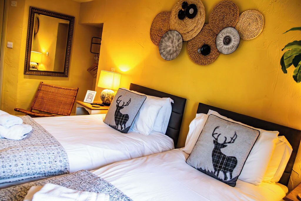 Une chambre d’hôtel avec deux lits, un miroir, une lampe et des éléments de décoration murale, notamment des paniers tressés et des coussins ornés de motifs de cerfs.