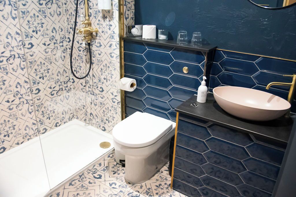 Ein Badezimmer mit Toilette in Weiß, einem weißen Waschbecken mit rosa Becken und einer Dusche mit goldfarbener Armatur.