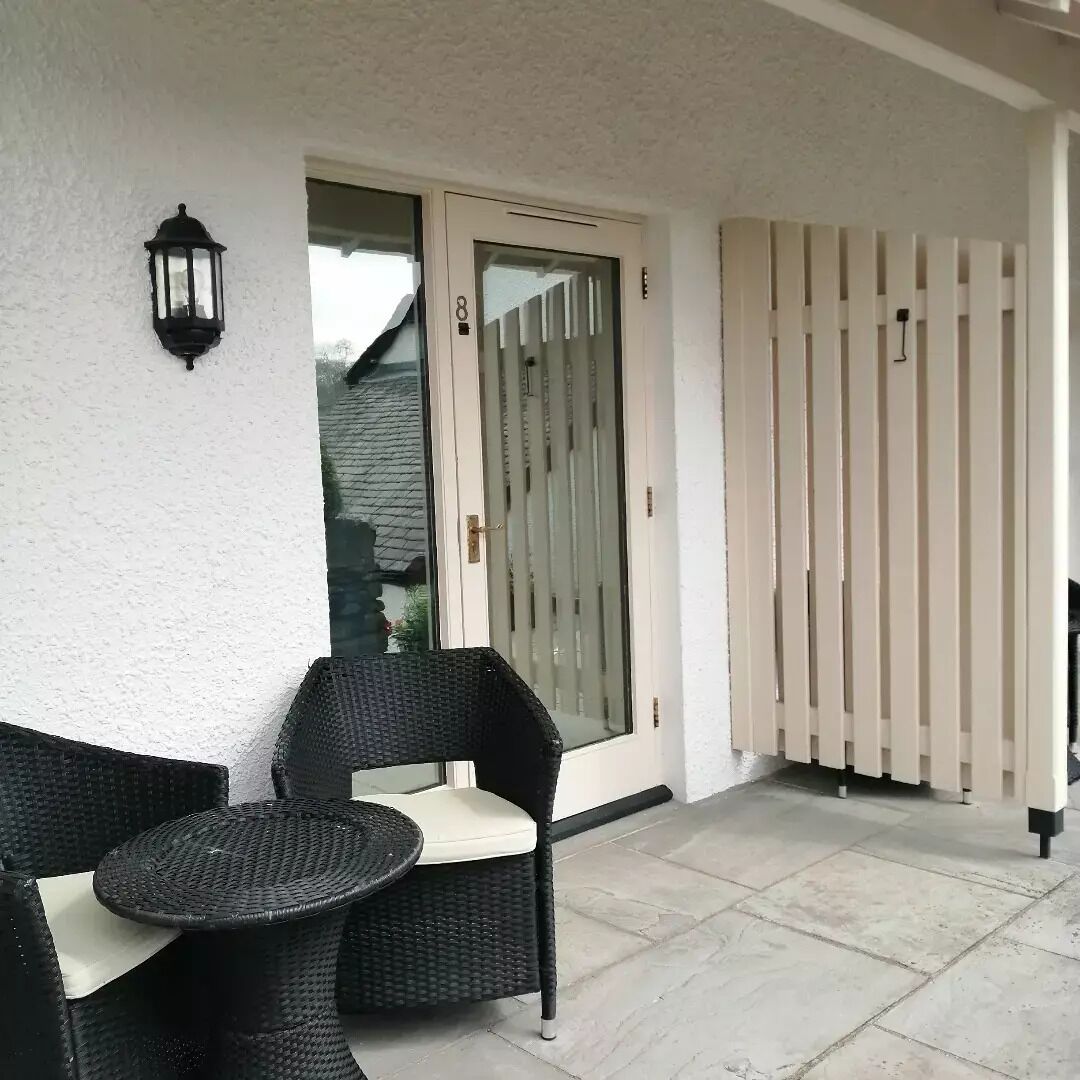 A balcony with wicker furniture, a glass door, and a white fence.