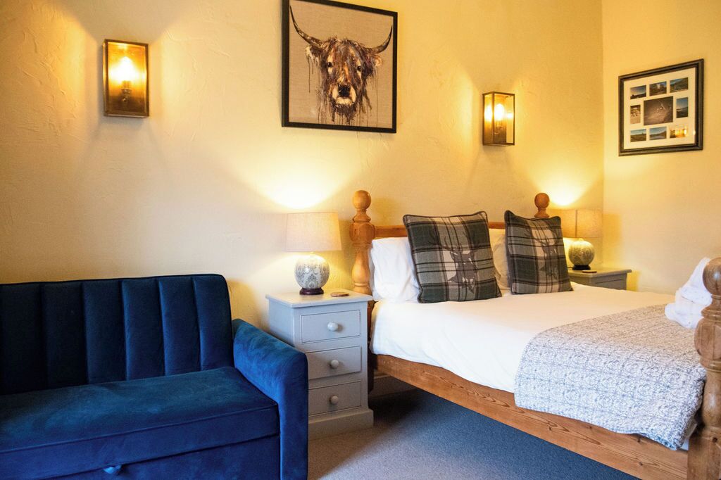 A bedroom with a bed, a nightstand, a lamp, a wall-mounted picture, and a blue sofa.