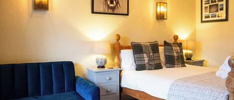 A bedroom with a bed, a nightstand, a lamp, a wall-mounted picture, and a blue sofa.
