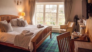 A hotel room with a bed, a chair, a desk, a lamp, a fan, and a window with curtains.