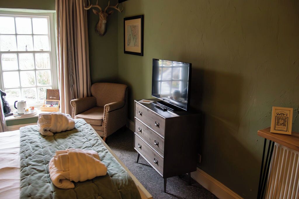 A room with a bed, a chair, a dresser, a television, and a window with curtains.