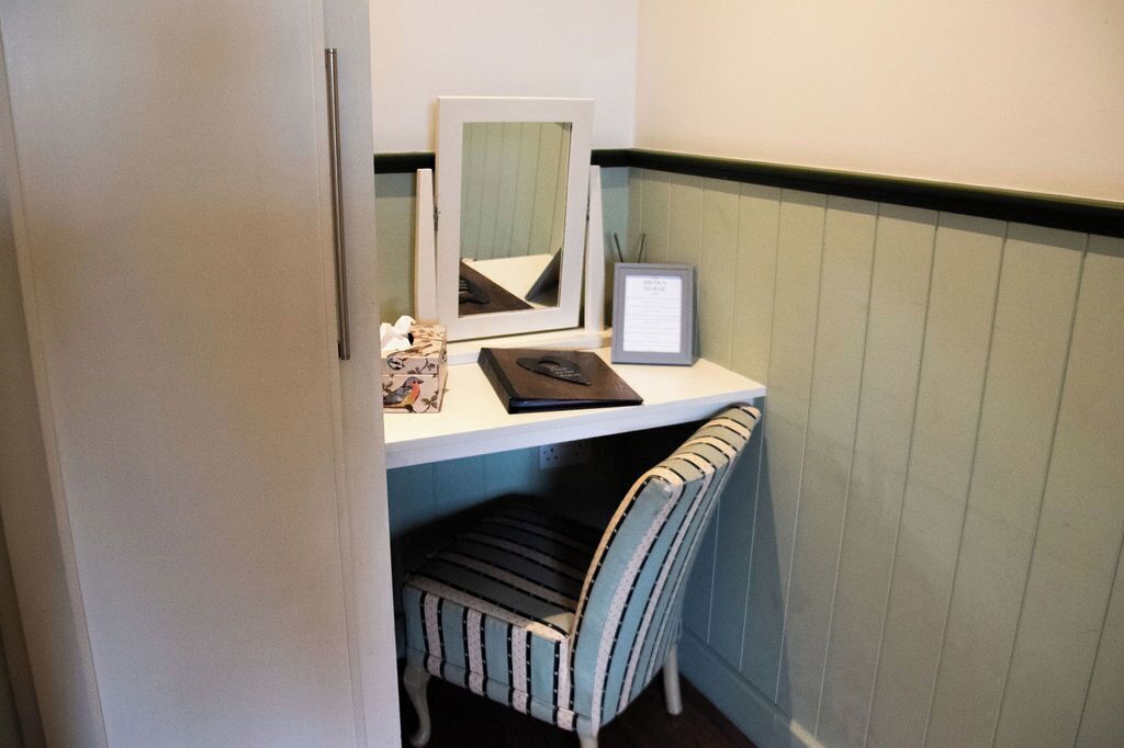 A small workspace with a desk, a framed mirror, a framed certificate, and a striped chair.
