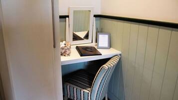 A small workspace with a desk, a framed mirror, a framed certificate, and a striped chair.