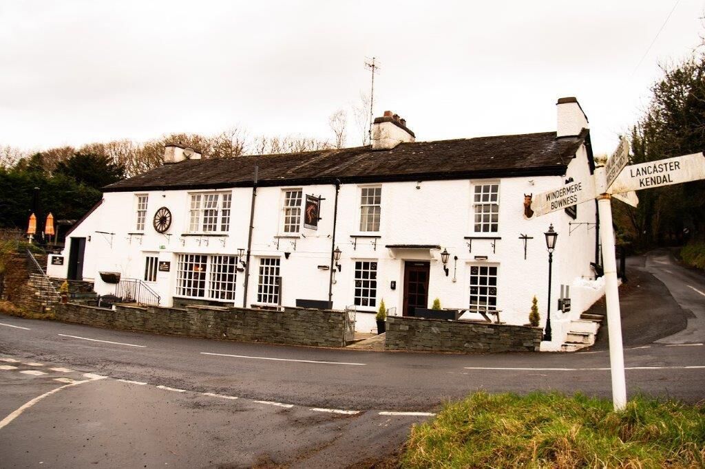A white building with a signboard indicating directions to Lancaster and Kendal.