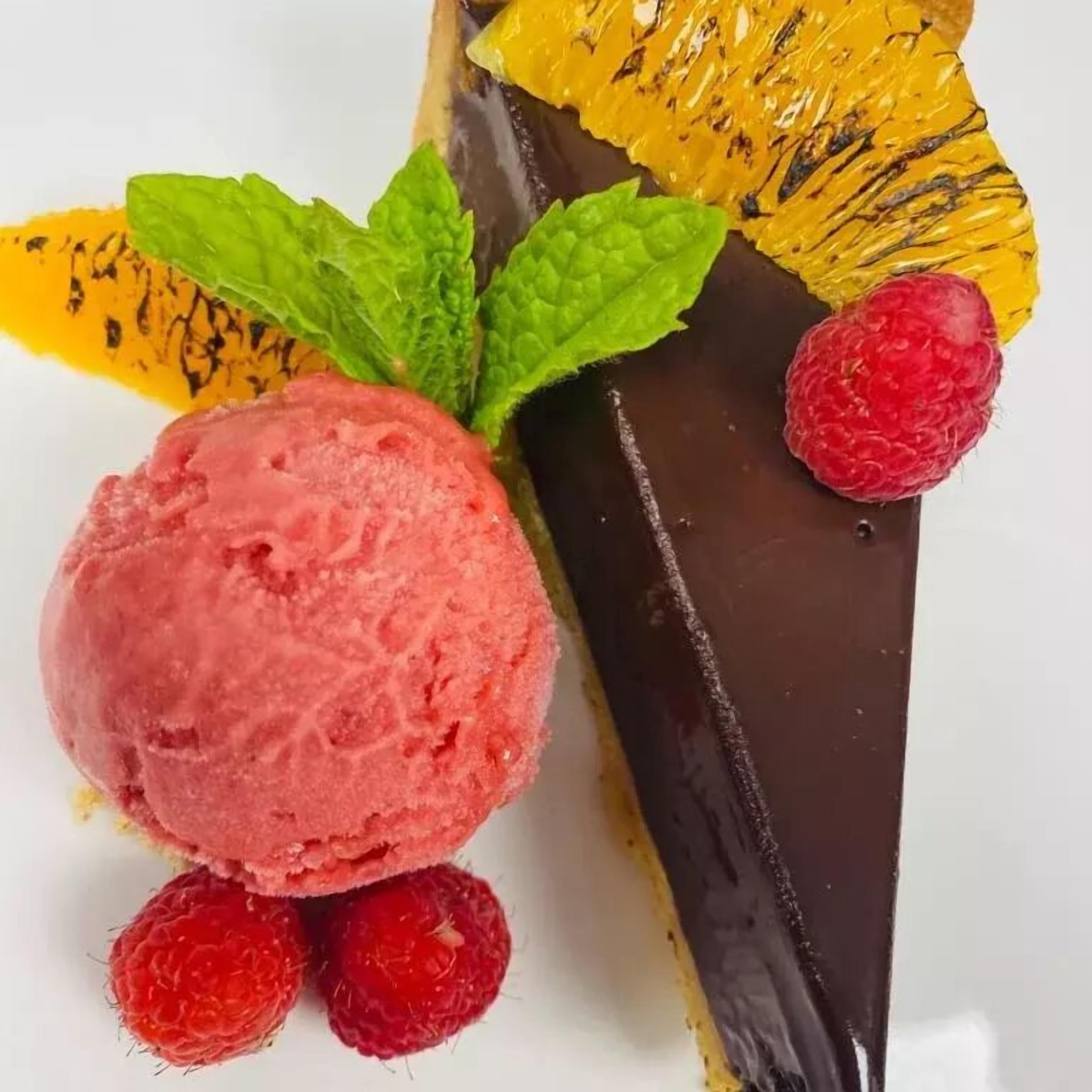 Un postre con helado, frambuesas y cobertura de chocolate.
