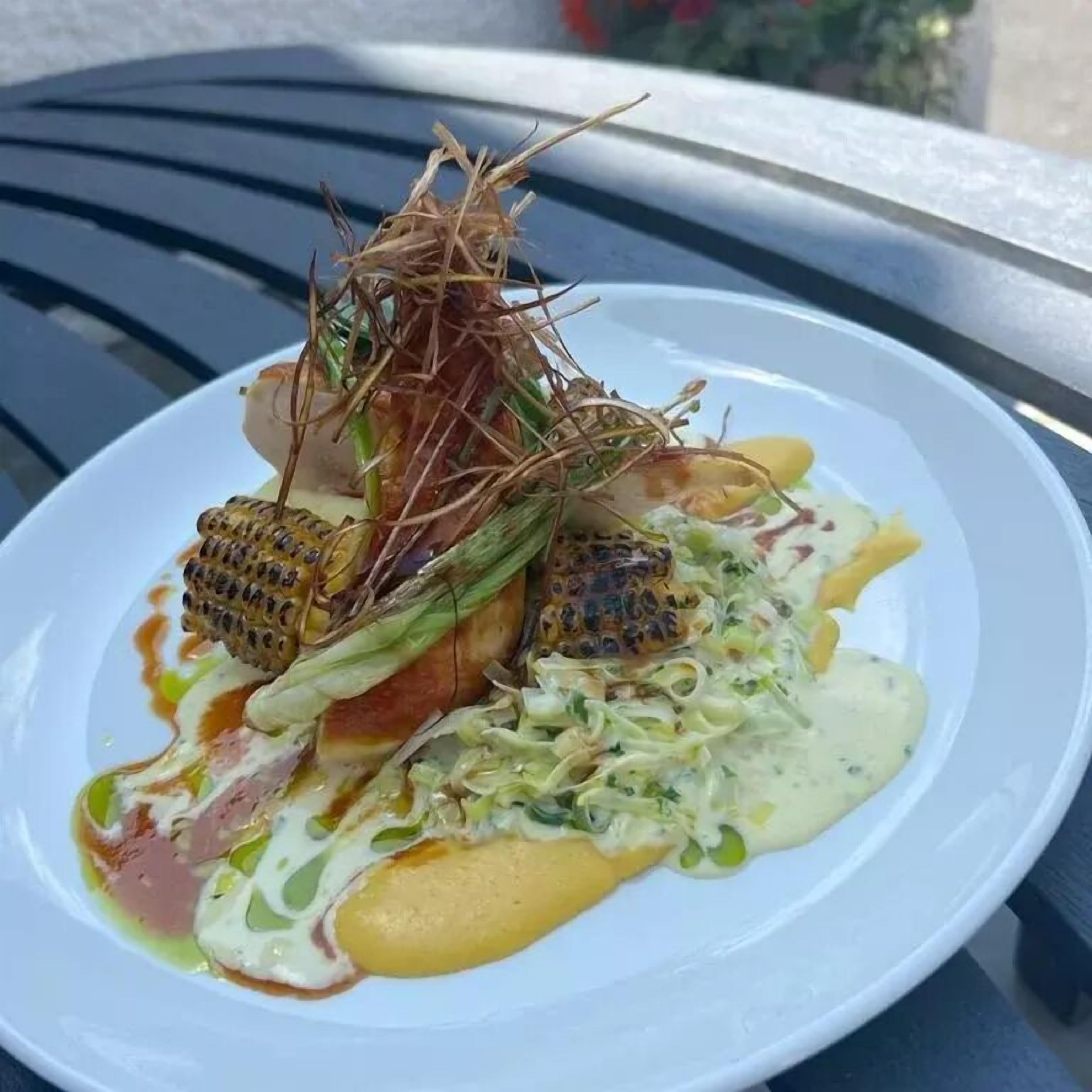 Ein weißer Teller mit einem Gericht aus gegrilltem Mais, Fleisch und Sauce.