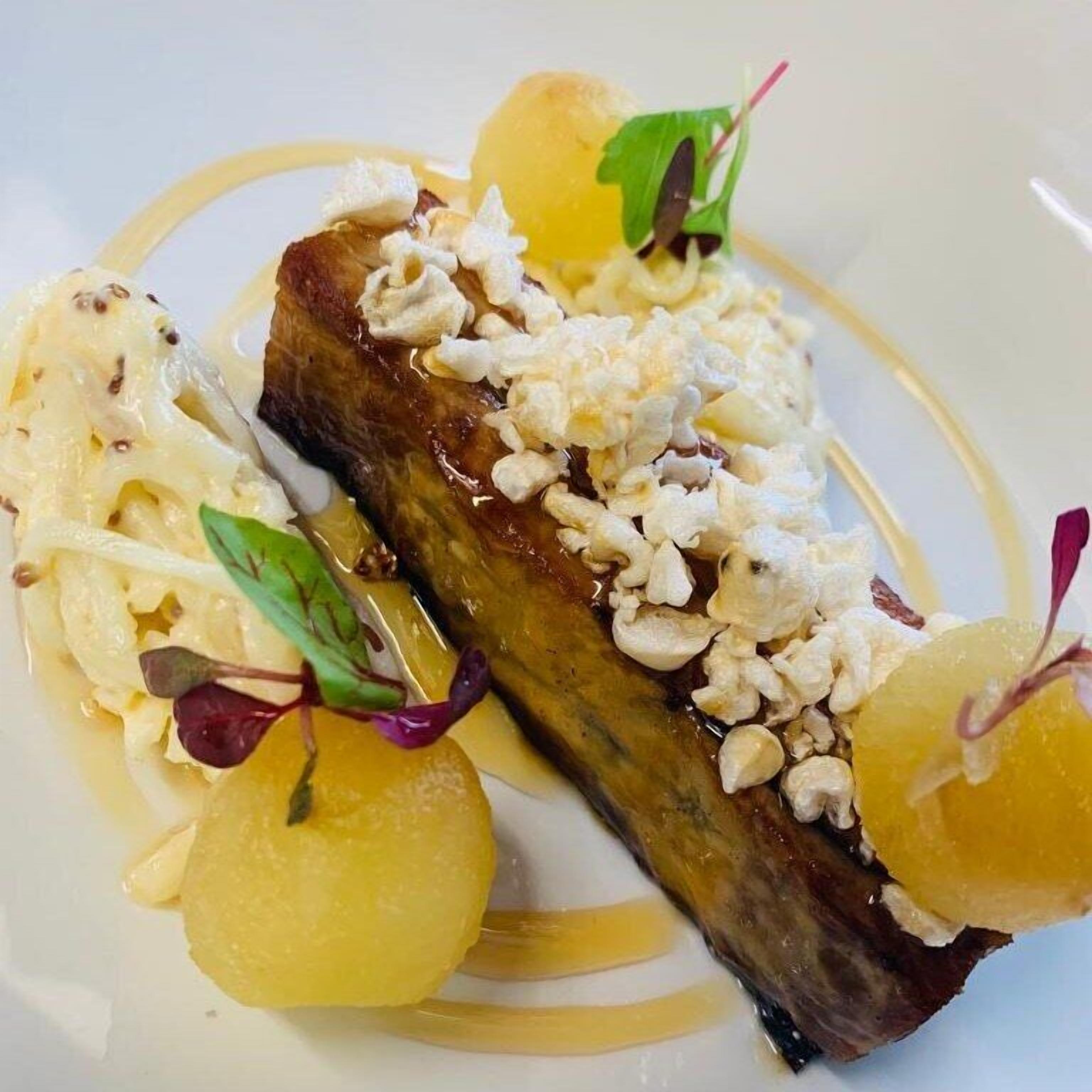 Un plato con carne, adornado con nueces y acompañado de esferas y vegetales verdes.