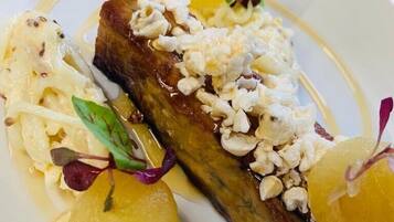 Un plato con carne, adornado con nueces y acompañado de esferas y vegetales verdes.
