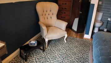 A room with a tufted armchair, a patterned rug, a wooden cabinet, and a blue ottoman.