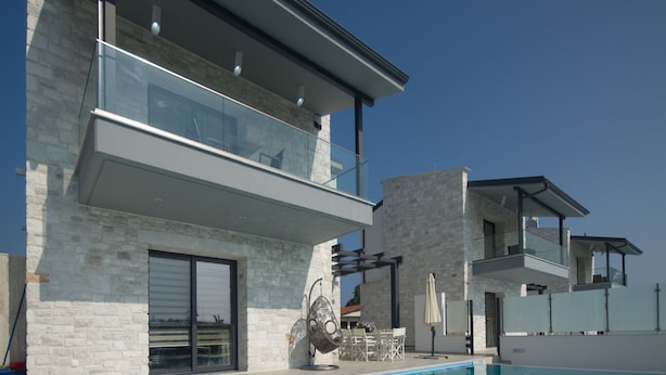 Una casa moderna de dos pisos con piscina, fachada de piedra y balcones de vidrio.